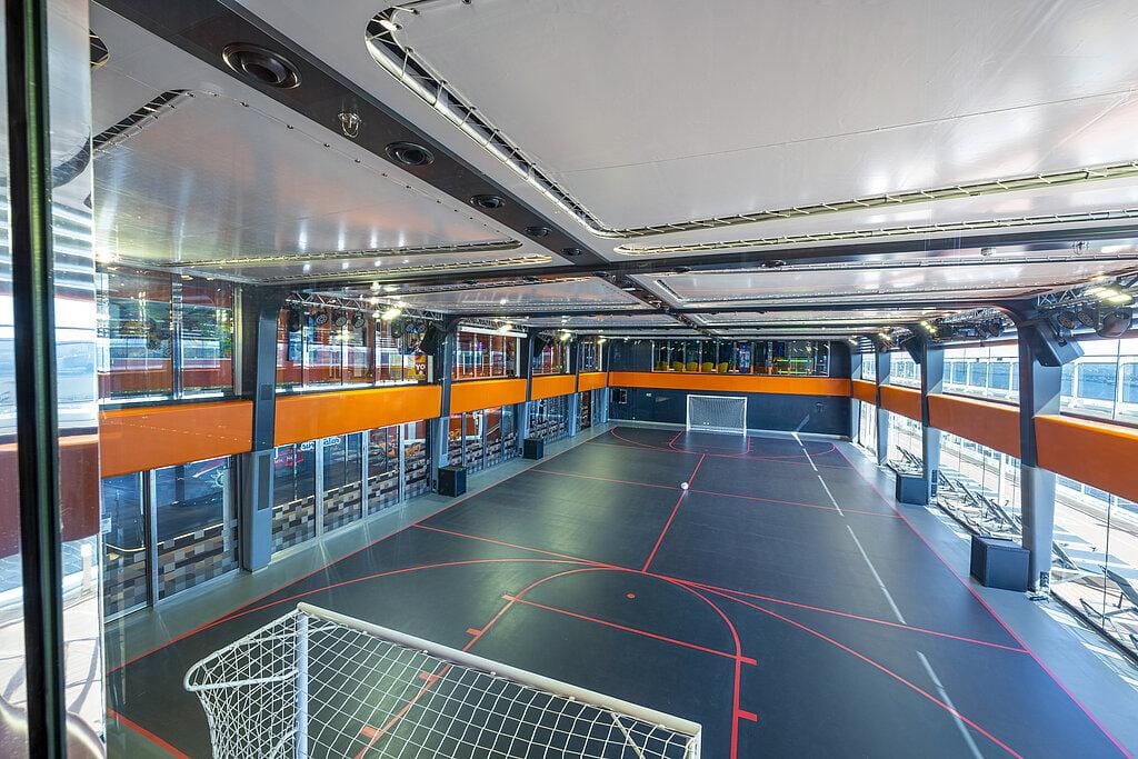 Moderne Sporthalle mit Glaswänden, orangenen Akzenten und kleinen Fußballtoren.