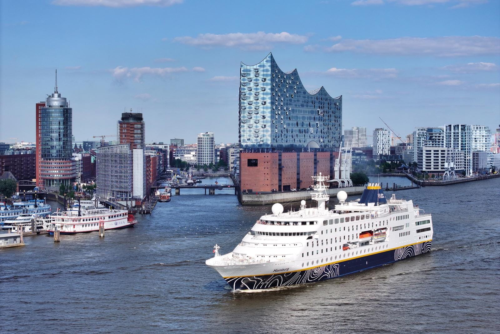 Kreuzfahrtschiff vor der Elbphilharmonie in Hamburg, Deutschland, bei strahlendem Sonnenschein.