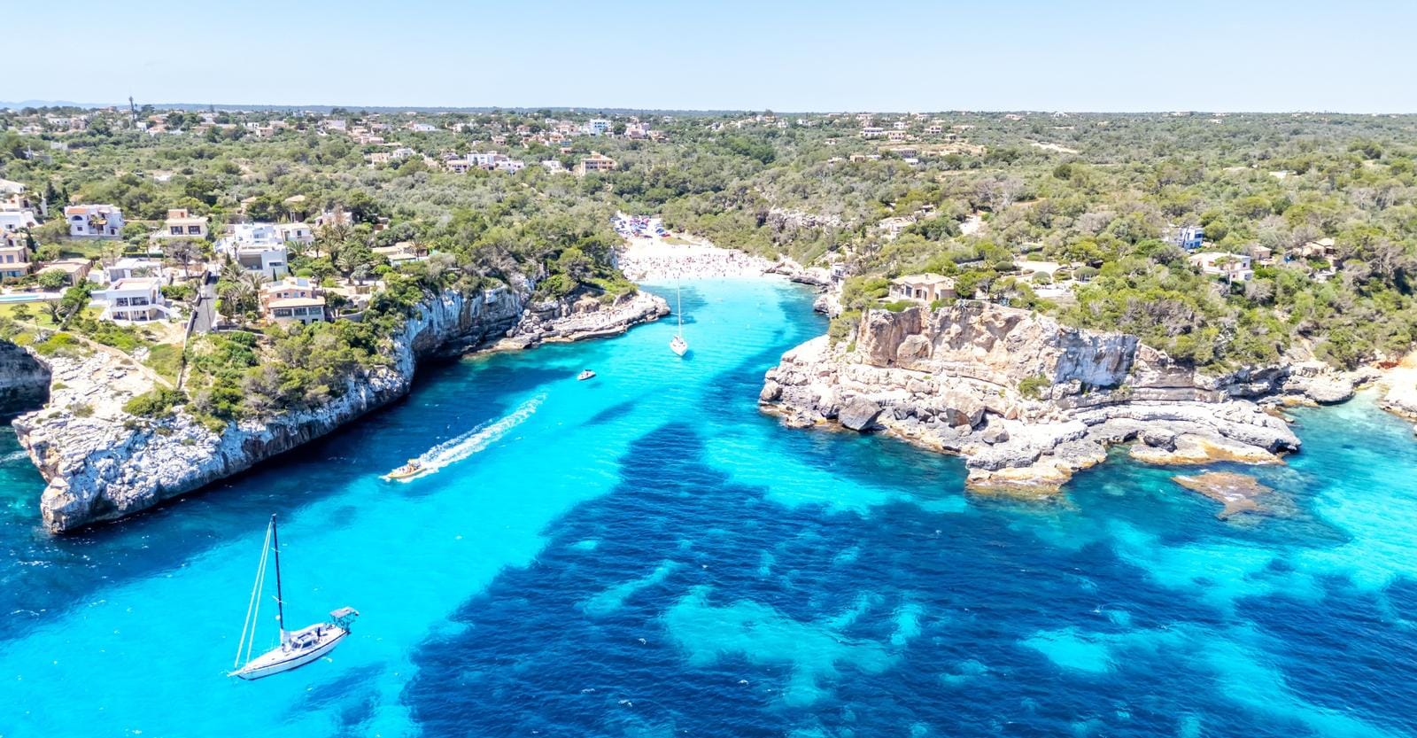 Türkisblaues Meer, felsige Küste und Boote nahe Steinstrand auf Mallorca, Spanien.