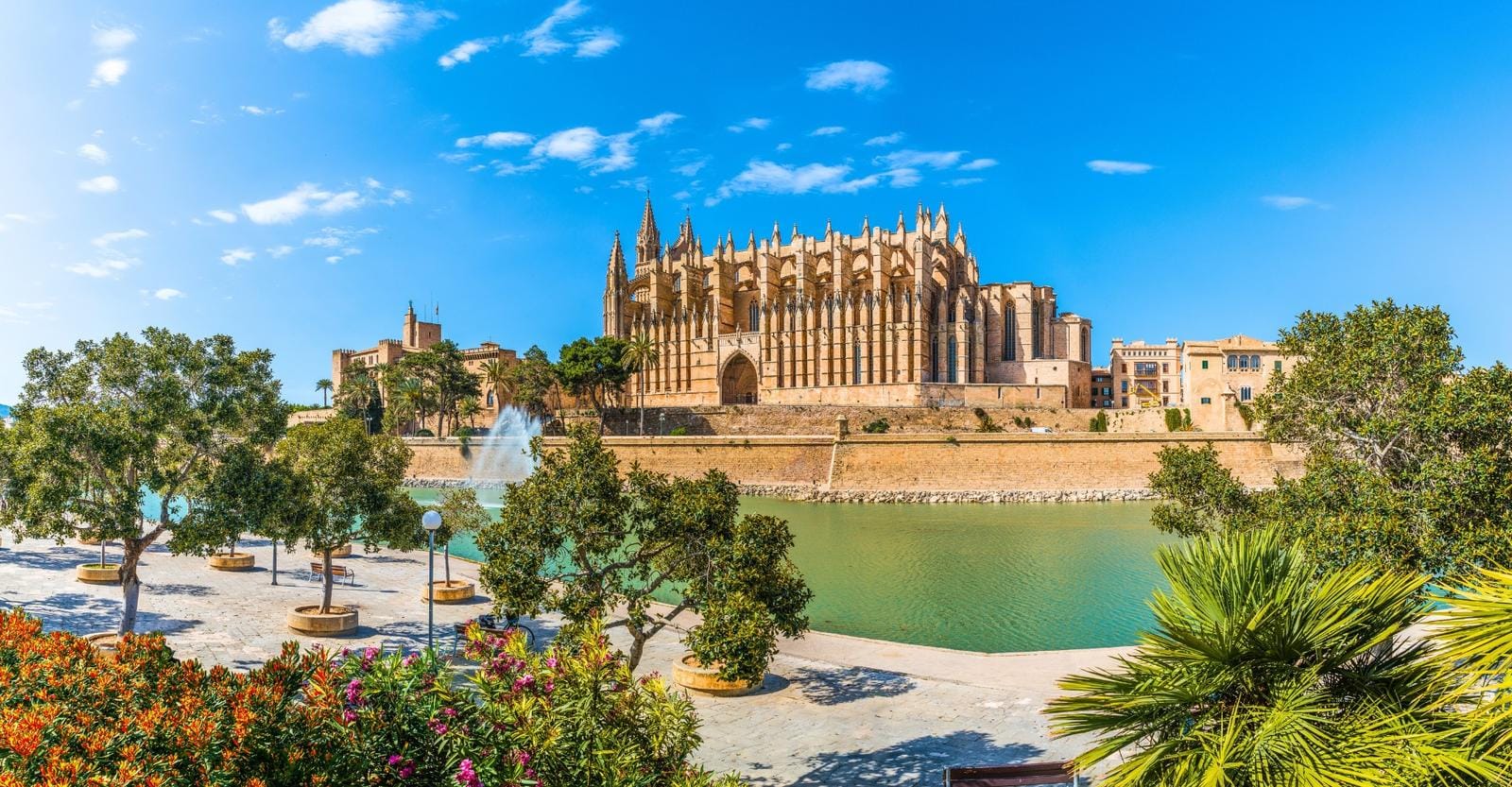 Gotische Kathedrale in Palma de Mallorca, vor blauem Himmel und blühenden Gärten.