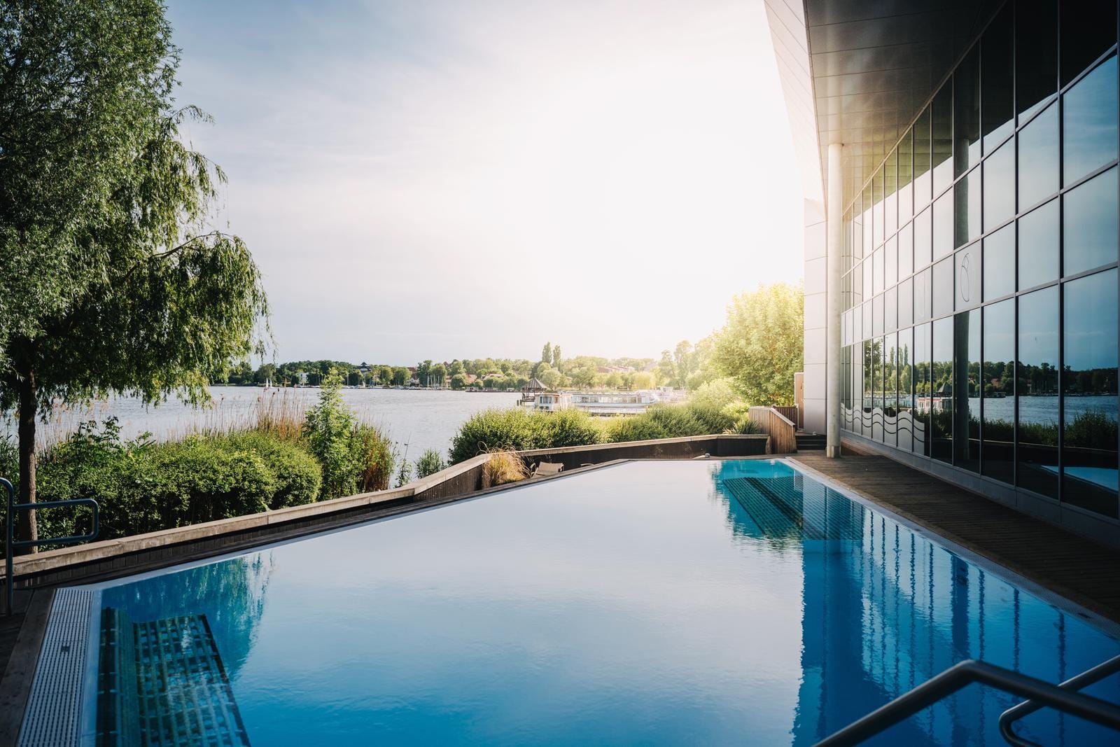 Hotel-Infinity-Pool am See bei Sonnenschein, umgeben von Bäumen und moderner Architektur.