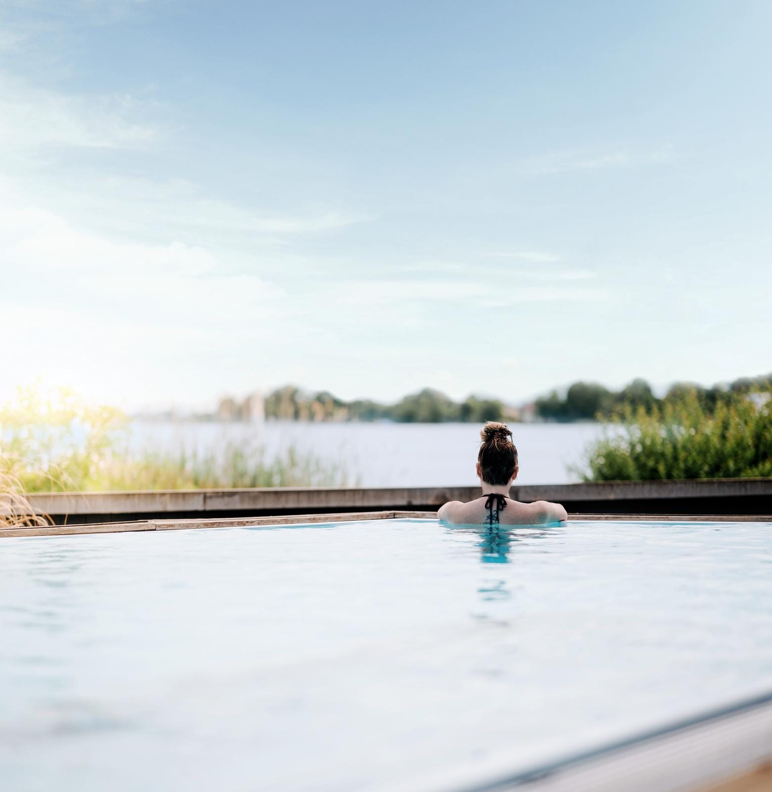 Frau entspannt im Infinity-Pool mit Blick auf einen See und bewaldete Landschaft.