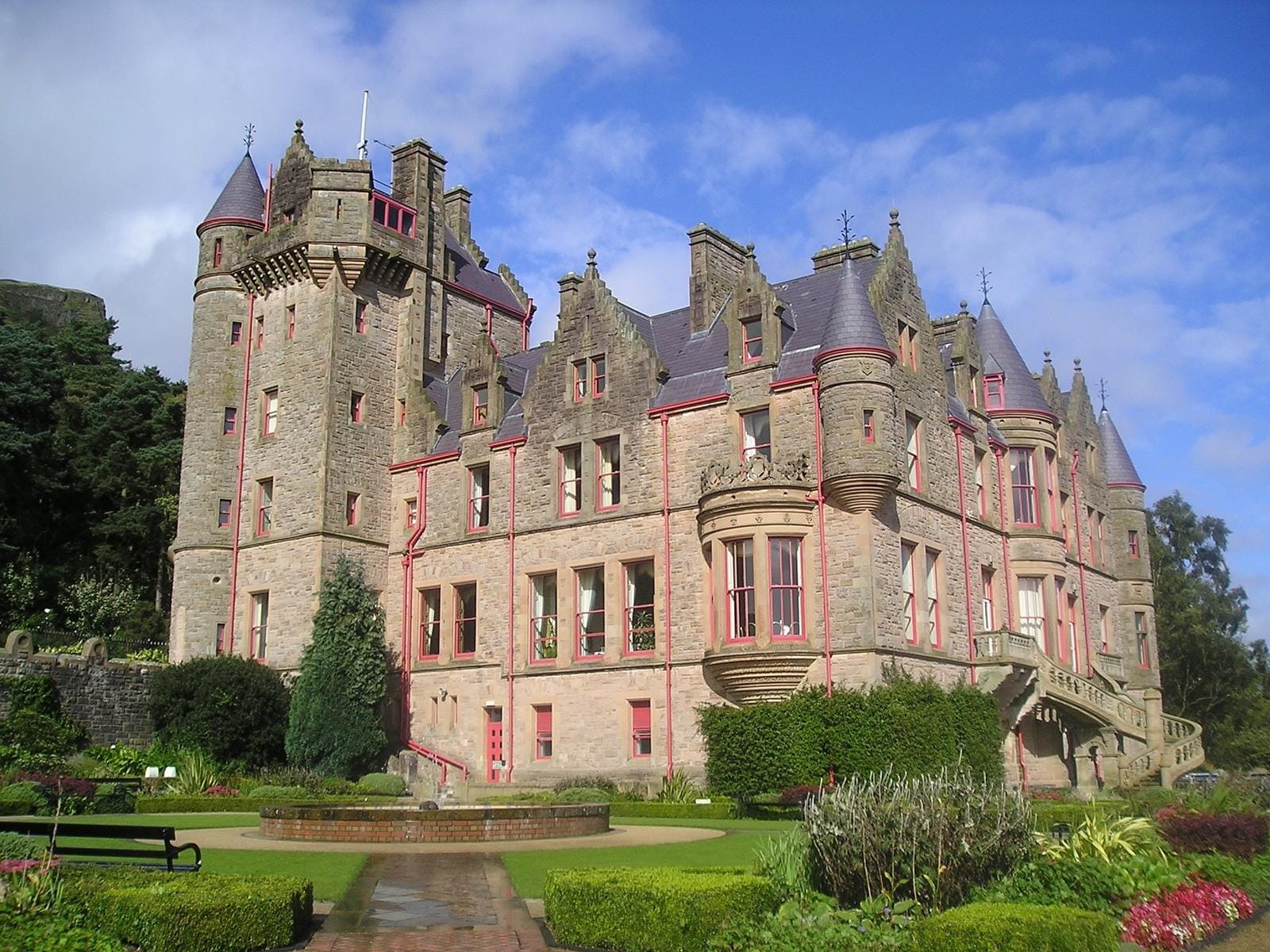 Sandstein-Schloss mit Türmen in gepflegtem Garten, unter blauem Himmel.