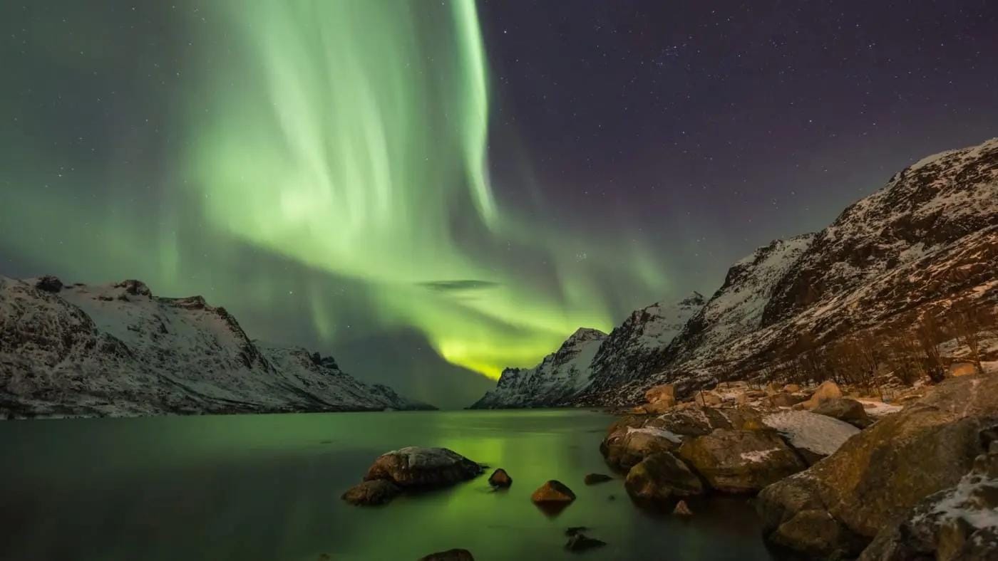 Nordlichter über verschneiten Bergen und See in Norwegen bei Nacht.