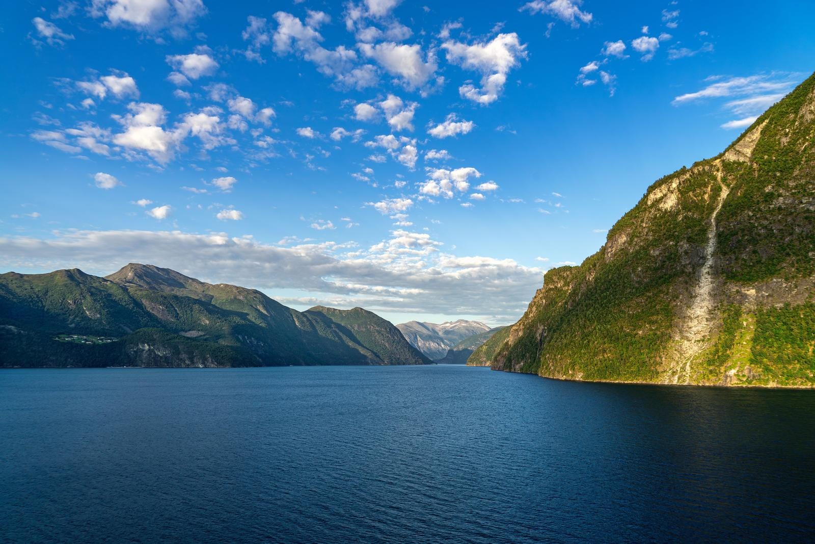 Norwegen Fjordlandschaft, tiefblaues Wasser und grüne Berge unter blauem Himmel.