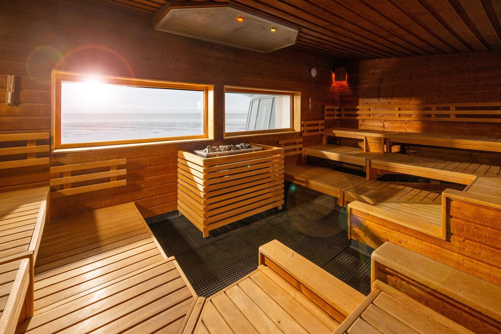 Moderne Sauna mit Holzbänken, großer Fensterblick auf Meer, warmes Ambiente.