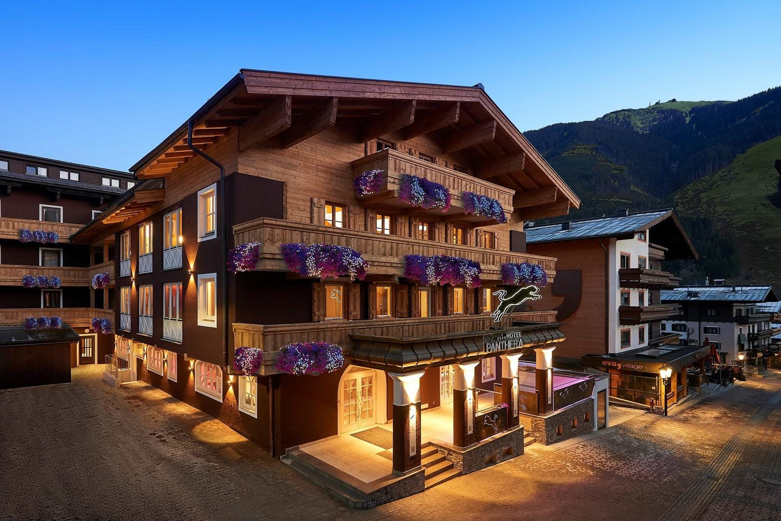 Alpenhotel in Österreich mit Balkonen voller Blumen, von Bergen umgeben bei Abenddämmerung.