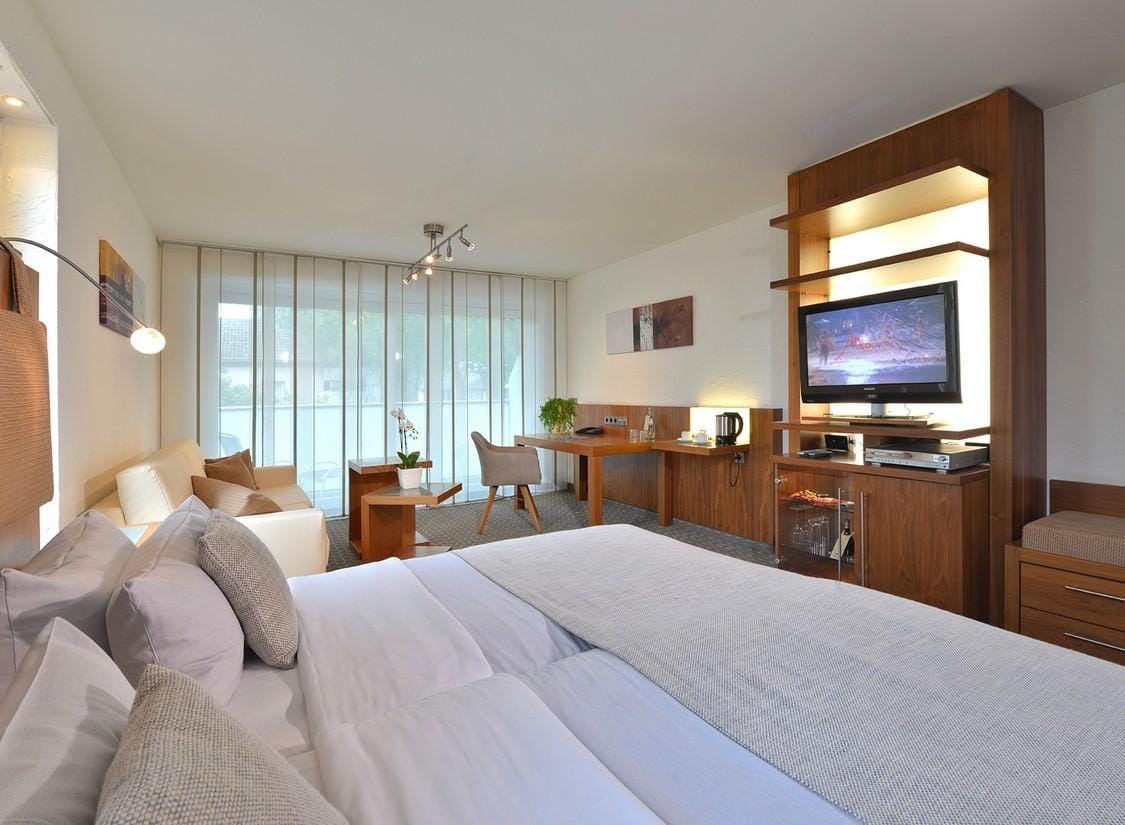 Modernes Hotelzimmer mit Doppelbett, Holzmöbeln, Schreibtisch und heller Atmosphäre.