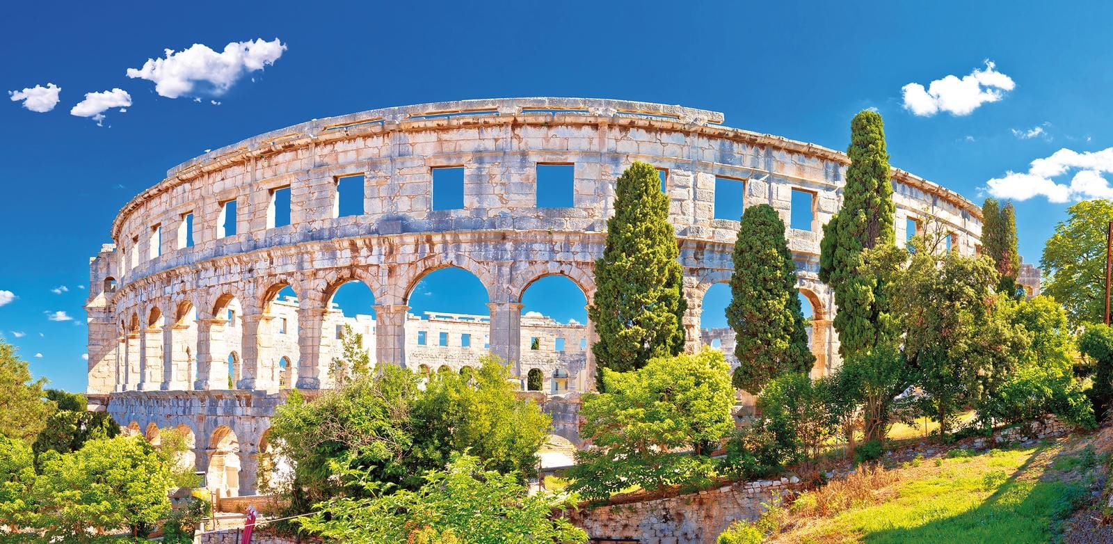 Römisches Amphitheater in Pula, Kroatien, umgeben von grünen Bäumen und blauem Himmel.