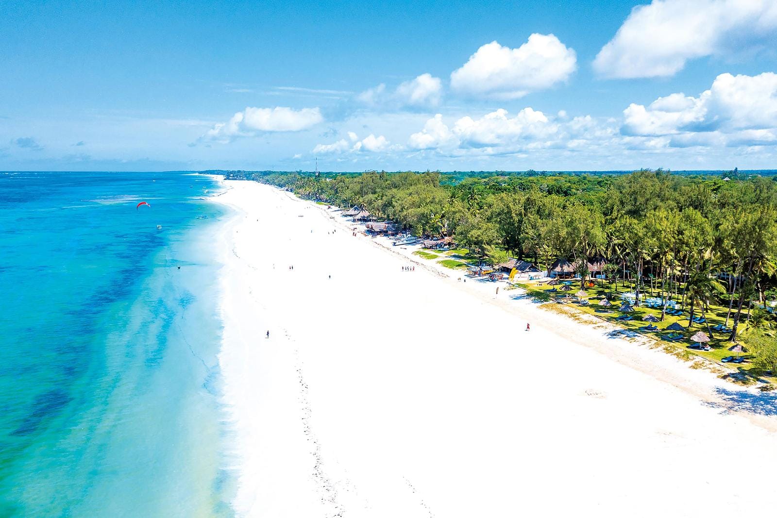 Weißer Sandstrand und türkisblaues Meer in Kenia, umgeben von grünen Palmen und klarem Himmel.