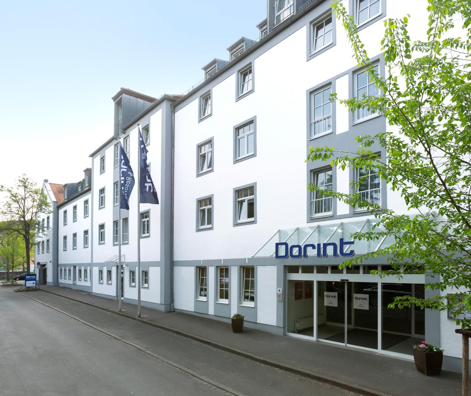 Weiße Hotel-Fassade mit grauen Akzenten, Glas-Eingang; modernes, helles Design.