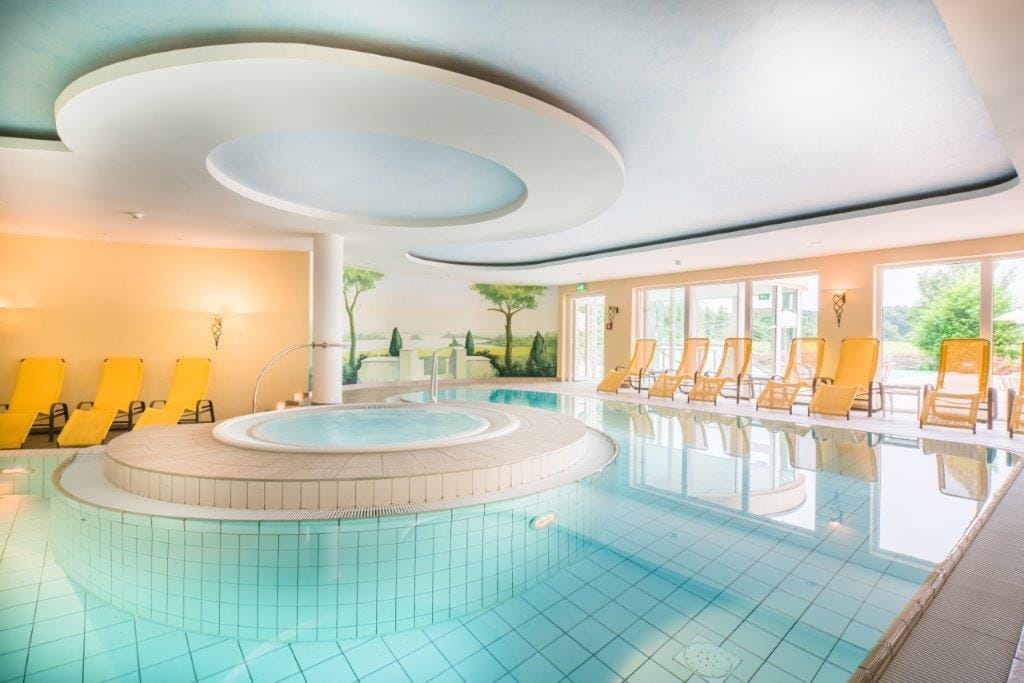Helles Hotel-Spa mit Innenpool, Whirlpool, gelben Liegestühlen und Wandmalerei.