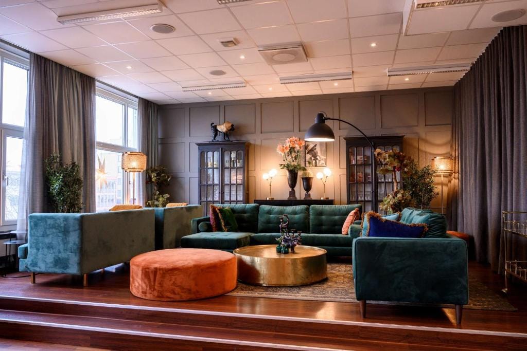 Gemütliche Hotel-Lounge mit grünen Sofas, großen Fenstern und eleganter Beleuchtung.