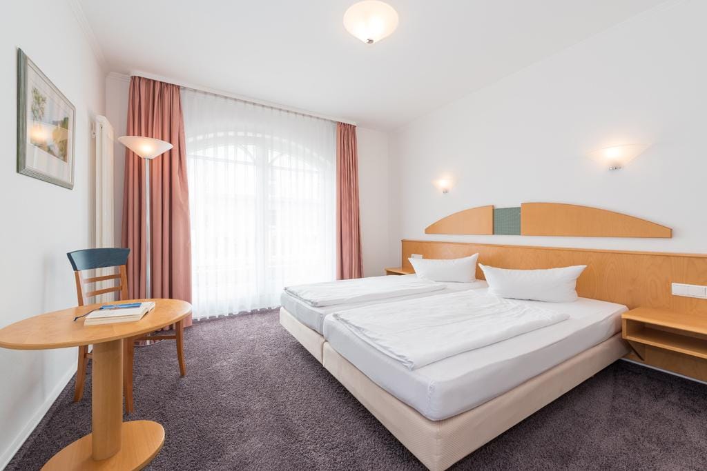 Helles Hotelzimmer mit Doppelbett, Holzdekor, Teppich, rosa Vorhängen, gemütlich.