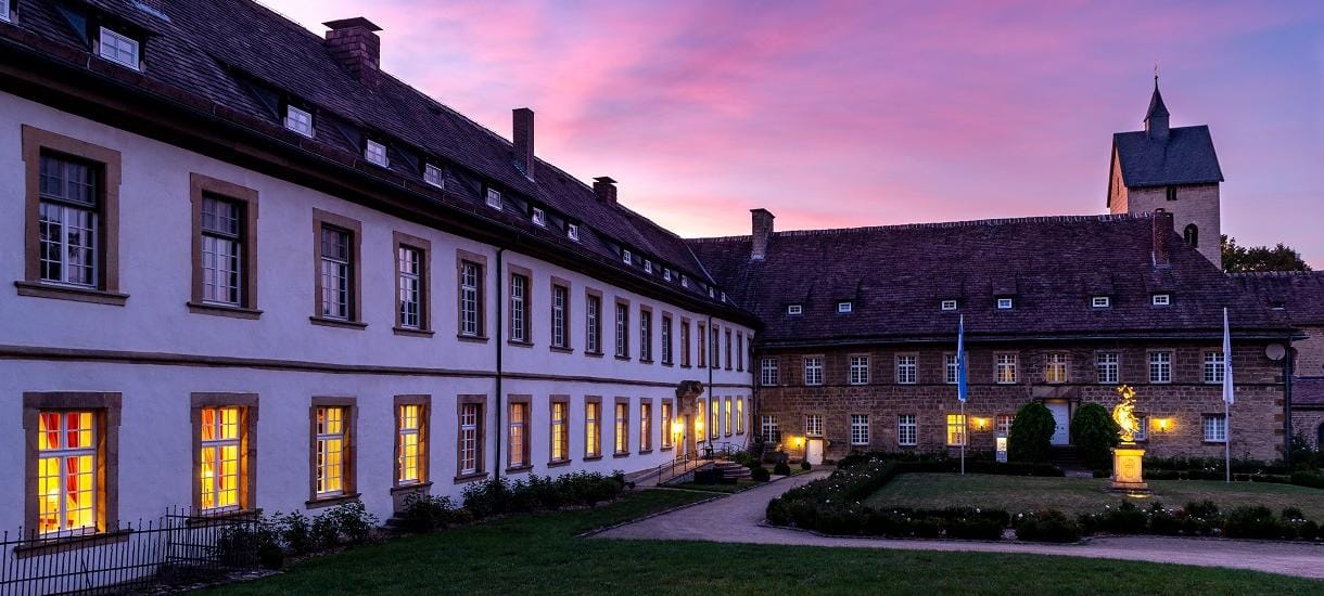 Historisches Gebäude bei Sonnenuntergang, erleuchtete Fenster, ruhige, idyllische Atmosphäre.