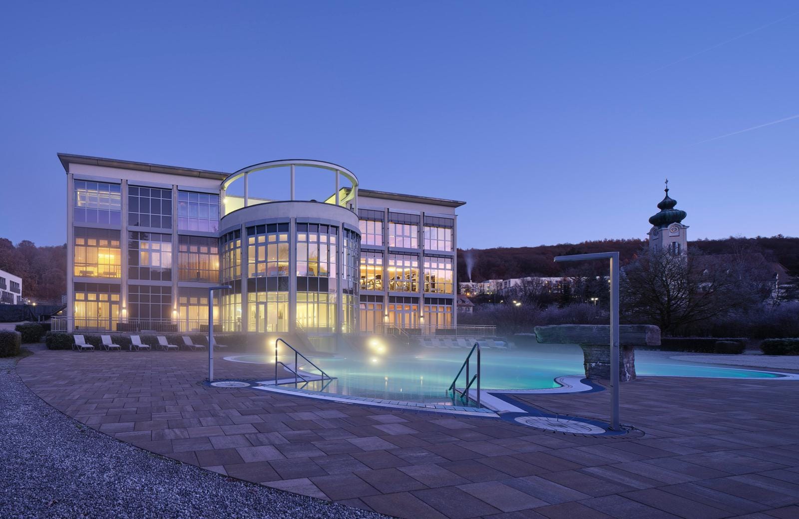 Modernes Hotel mit beleuchtetem Außenpool bei Abenddämmerung, ruhige Atmosphäre.