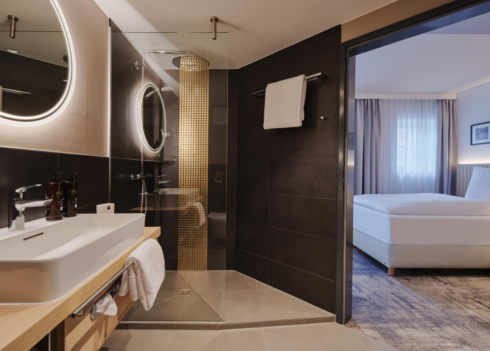 Modernes Hotelzimmer mit elegantem Bad, goldenen Akzenten, Dusche und großem Bett.