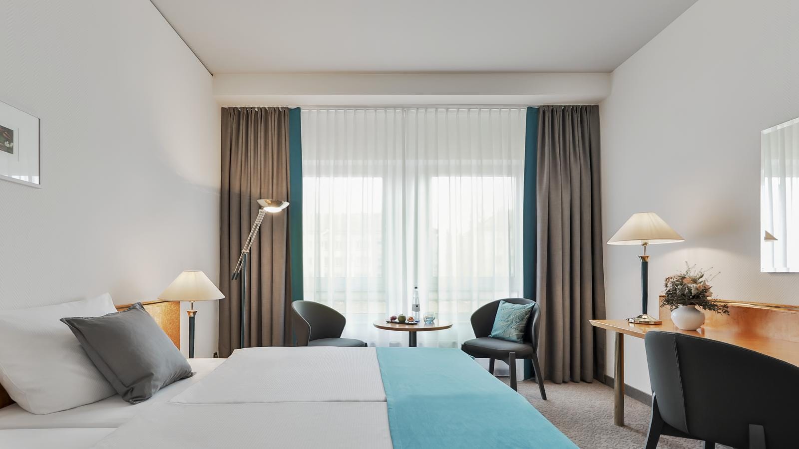 Helles Hotelzimmer mit modernen Möbeln, Doppelbett, blauen Akzenten und Sitzbereich.