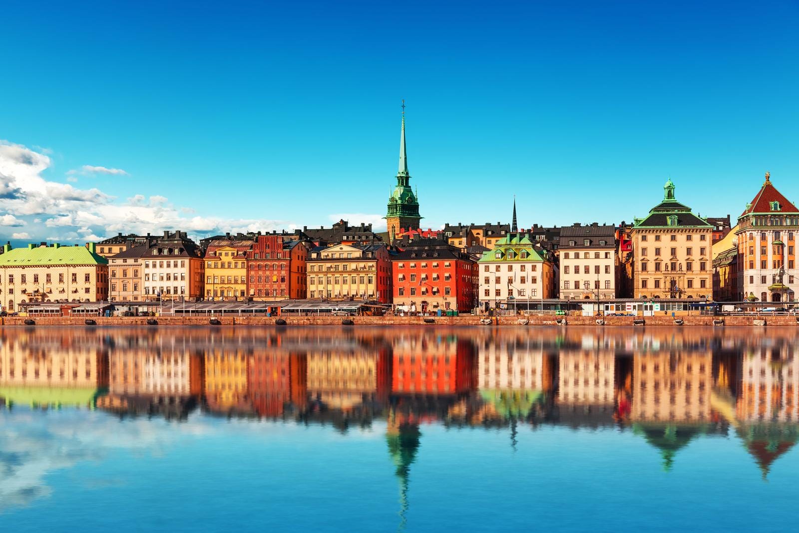 Bunte Altstadtfassaden und Kirchen in Stockholm, Schweden spiegeln sich im Wasser.