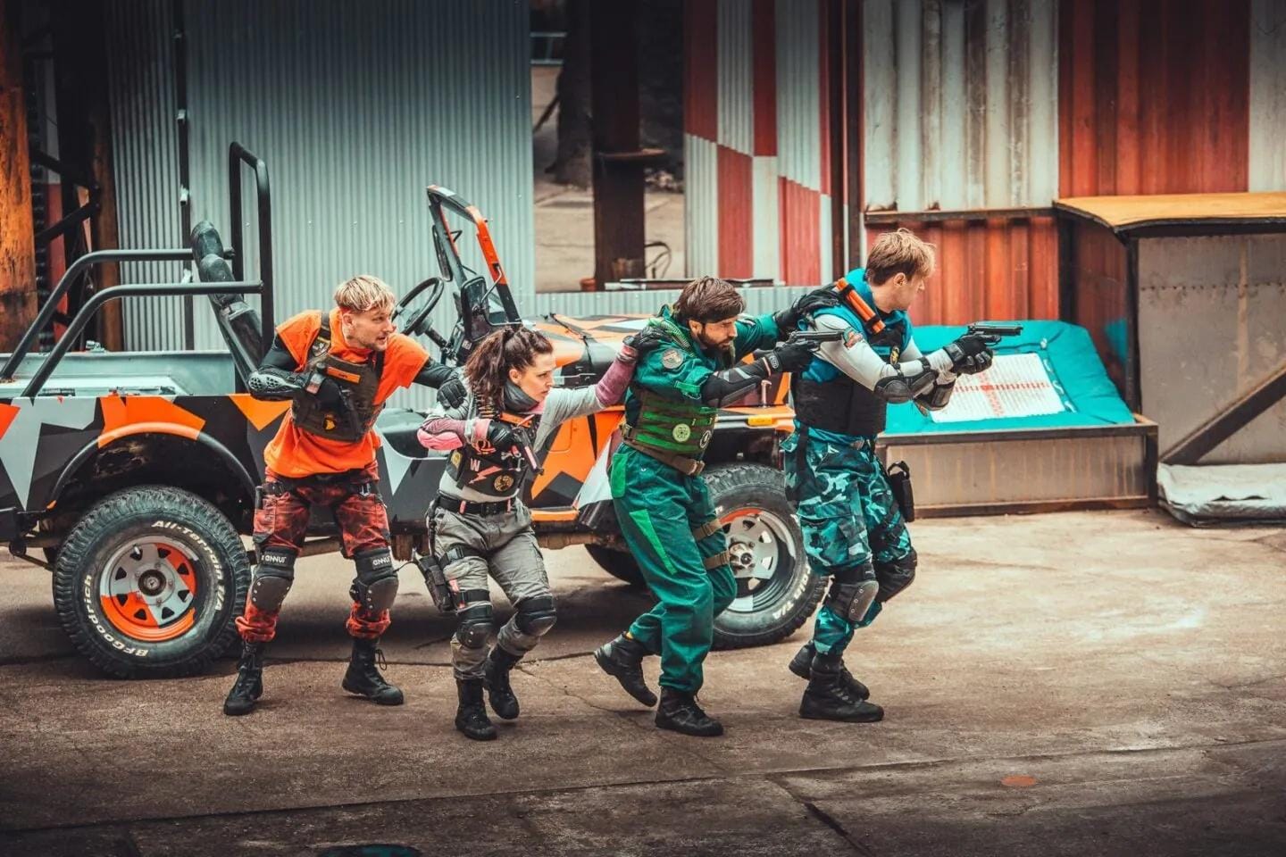 Vier Personen in taktischen Outfits vor einem bunten Geländewagen.