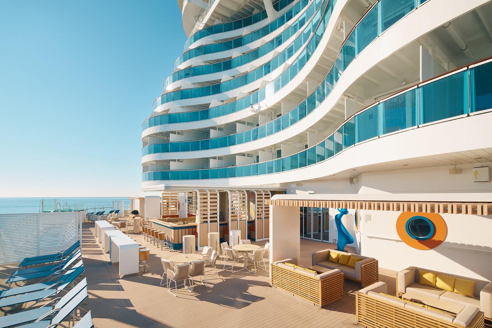 Moderne Kreuzfahrt-Lounge, geschwungene Balkone, blaue Glasfronten, sonnige Atmosphäre.