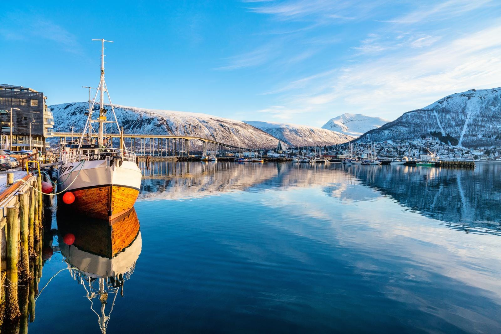 Verschneite Hafenstadt in Norwegen, ruhig reflektiert im klaren blauen Wasser.