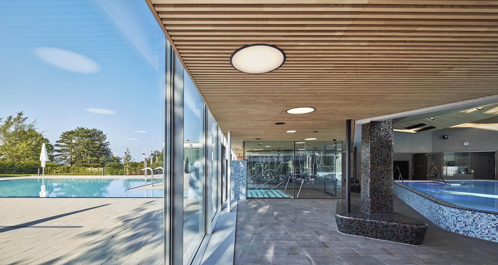 Moderner Spa-Bereich mit Innen- und Außenpool, helle Holzdecke, große Fenster.