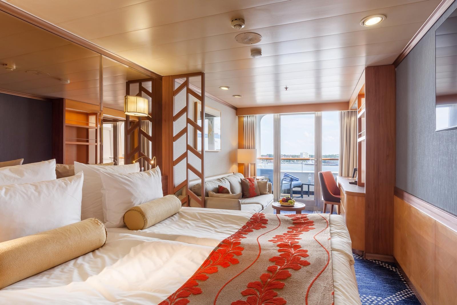 Elegantes Hotelzimmer mit Balkon, Sofaecke, warmen Holztönen und maritimer Deko.