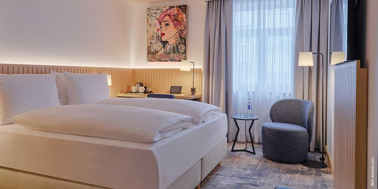 Modernes Hotelzimmer mit Doppelbett, Kunstwerk, Schreibtisch, Sessel und sanfter Beleuchtung.
