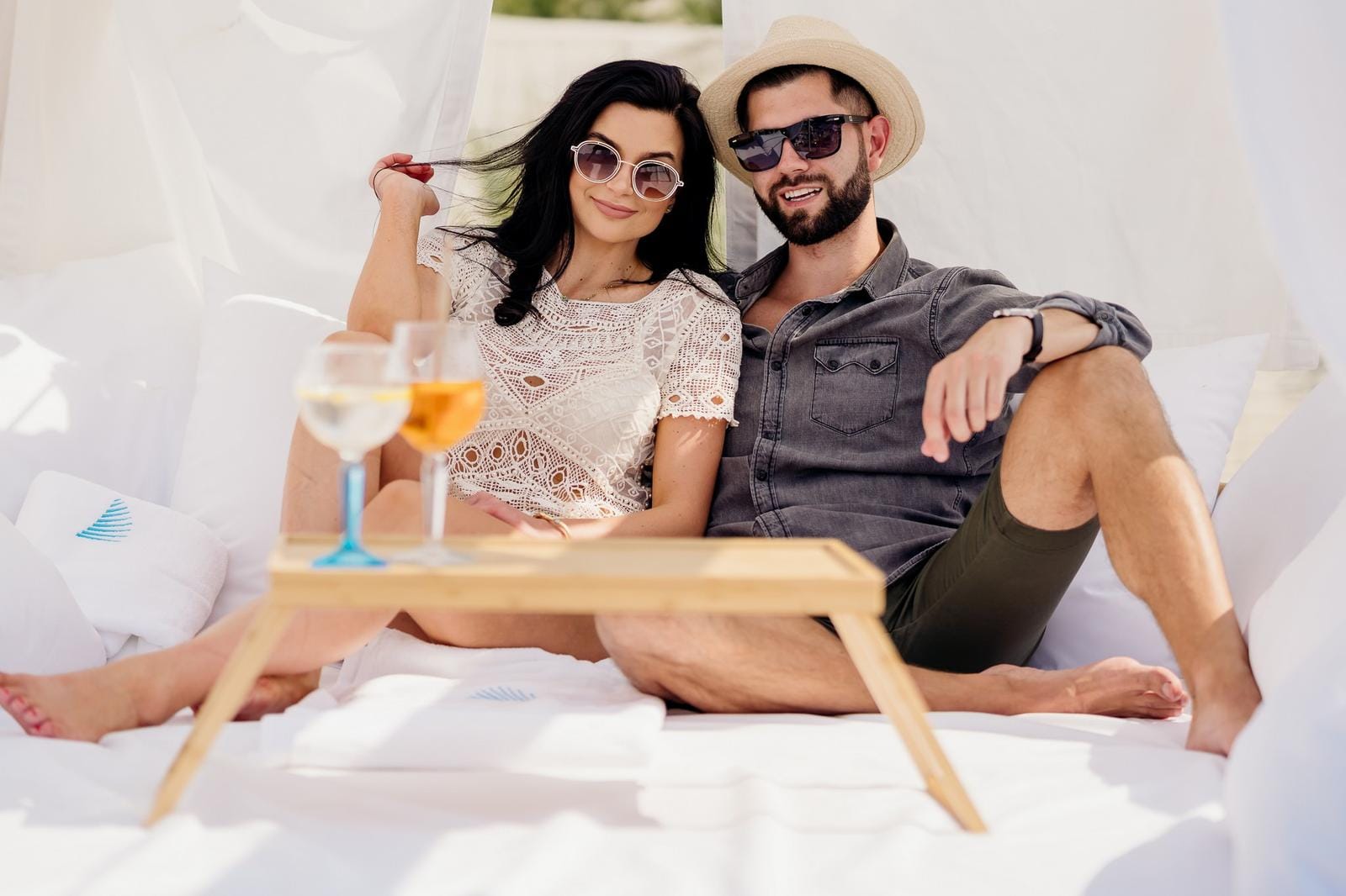 Paar entspannt auf weißem Daybed unter Sonnenschutz mit Cocktails, sommerlich-modern.