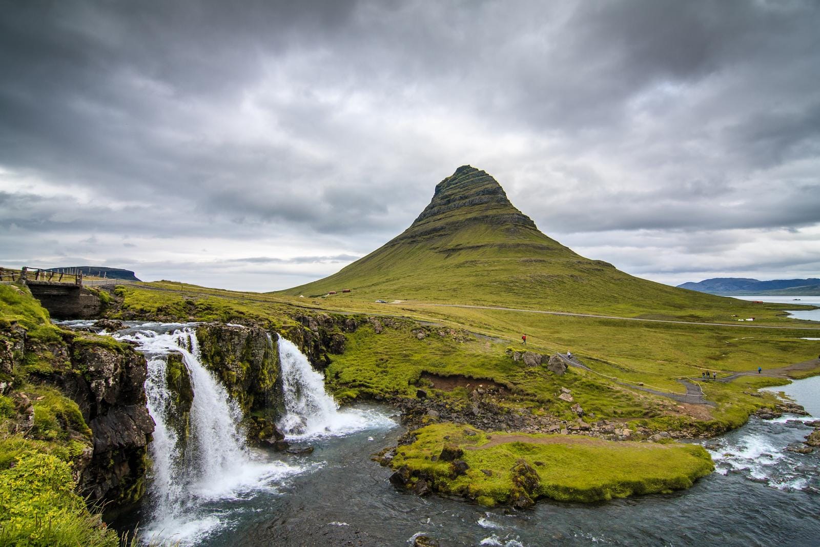 Berg Kirkjufell in Island, mit Wasserfall im Vordergrund, dramatischer Wolkenhimmel.