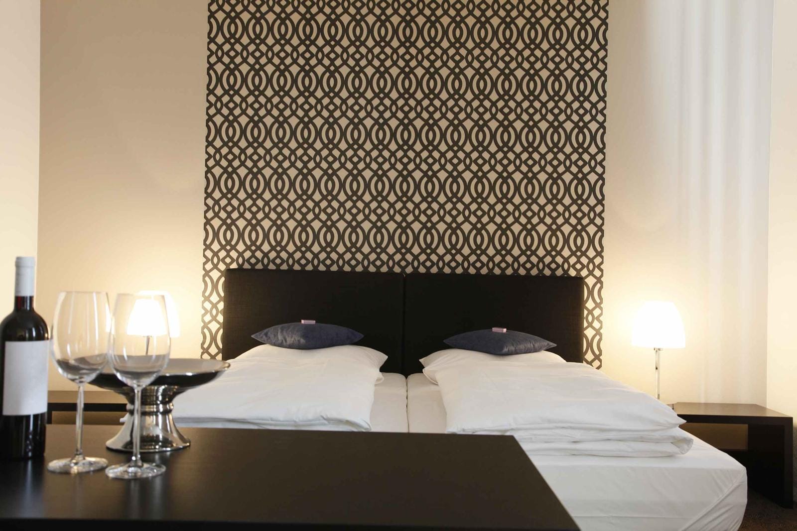 Modernes Hotelzimmer mit Doppelbett, geometrischer Tapete und gemütlicher Beleuchtung.