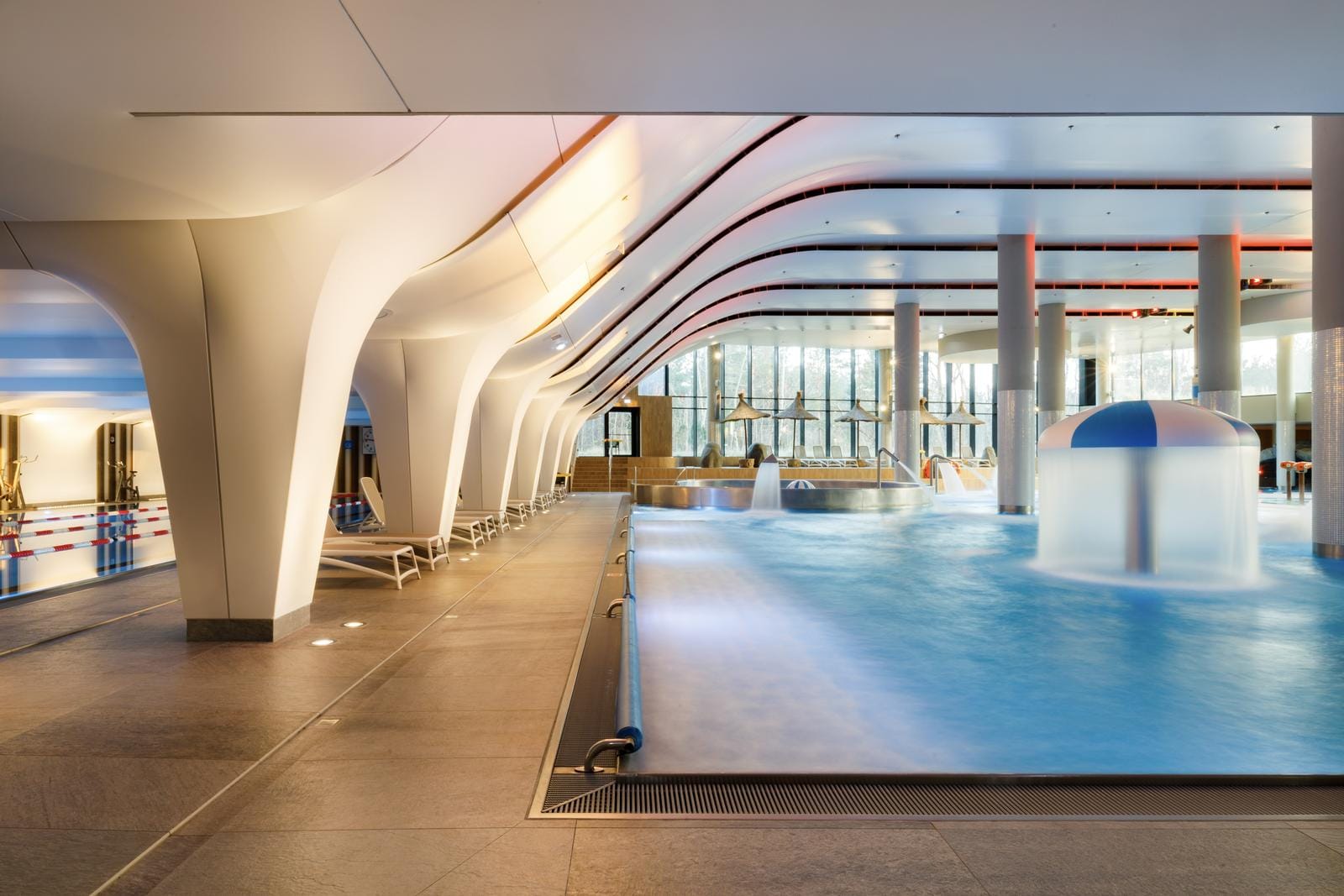Modernes Hotel-Spa mit großem Pool, stilvollen Liegen und sanfter Beleuchtung.