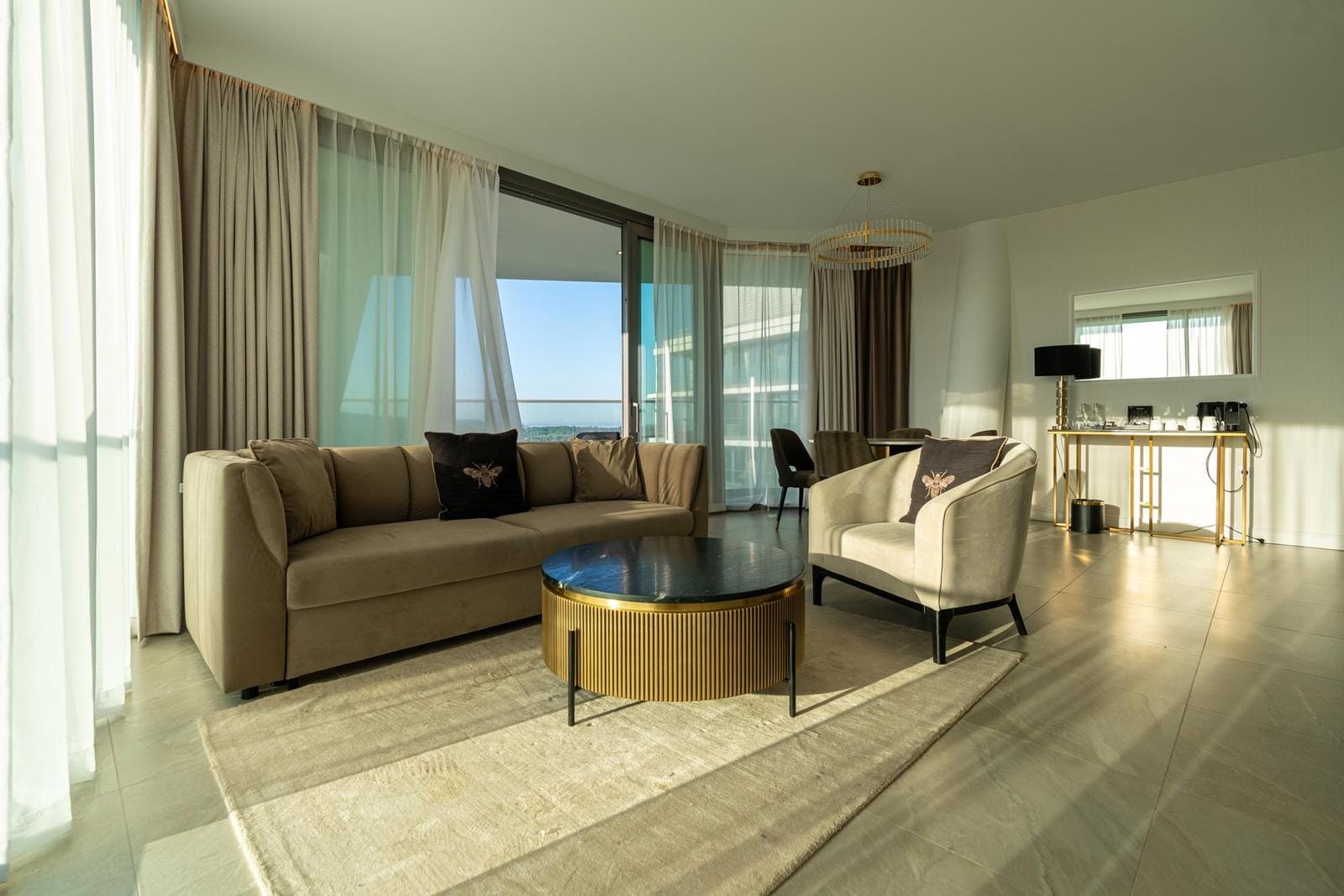 Elegante Hotelsuite mit heller Einrichtung, Meerblick, beiger Couch und goldenen Akzenten.