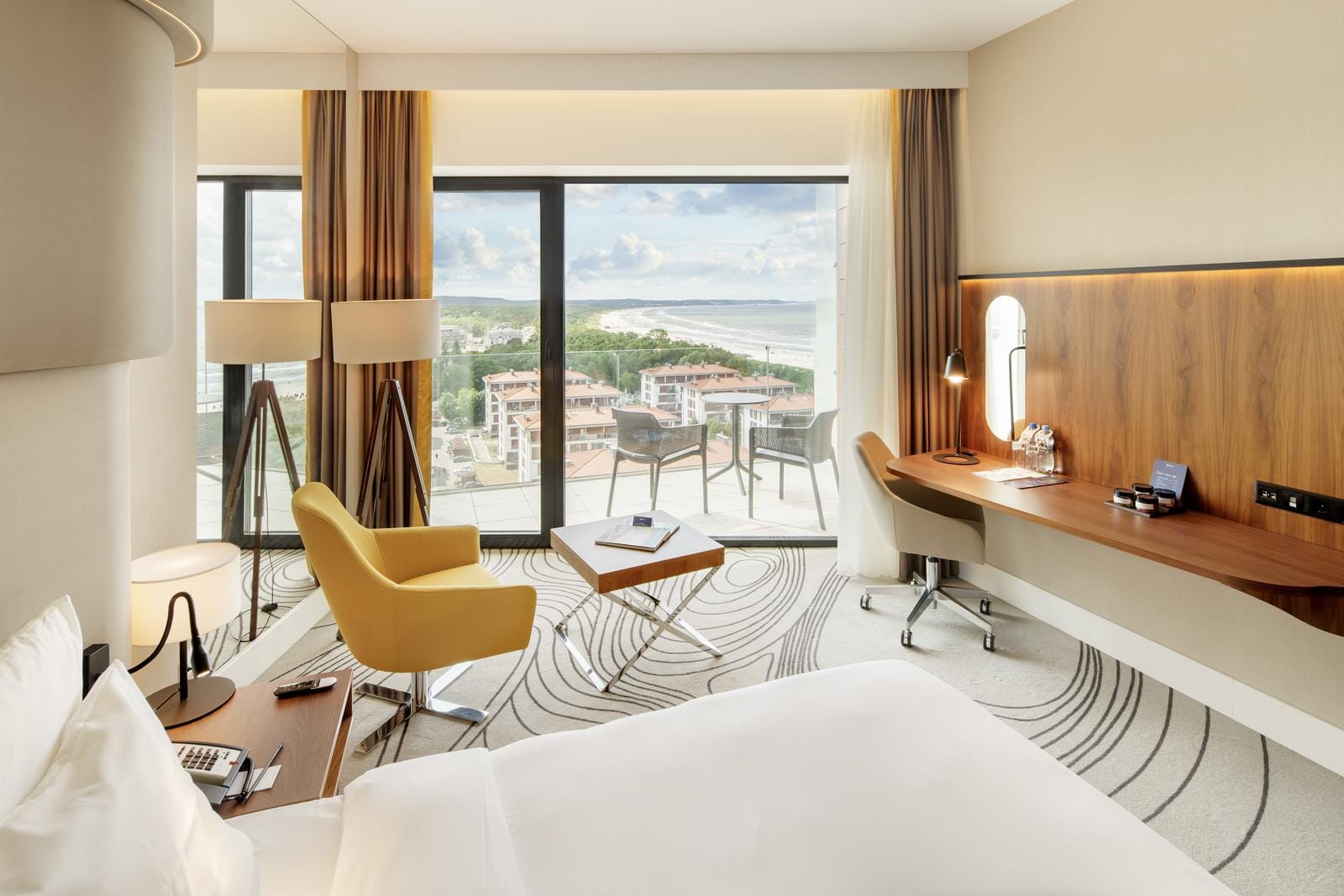 Modernes Hotelzimmer mit Meerblick, Sessel, Schreibtisch, helle Farben, großes Fenster.
