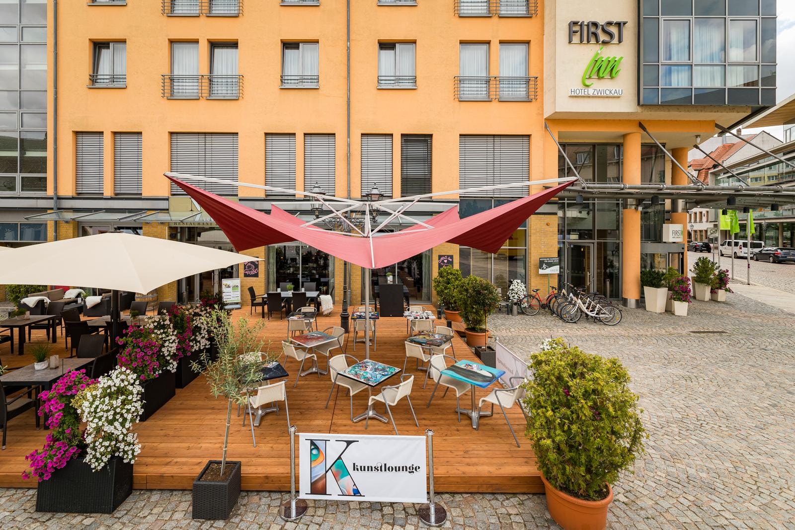 Außenterrasse eines Hotels in Zwickau mit bunten Sonnensegeln und Blumenarrangement.