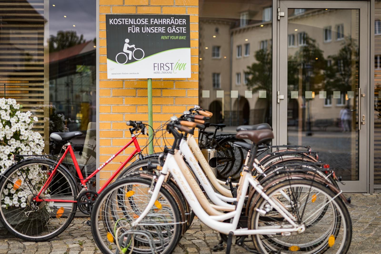 Fahrräder vor einem Hotel mit gelber Backsteinmauer und Schild "Kostenlose Fahrräder".