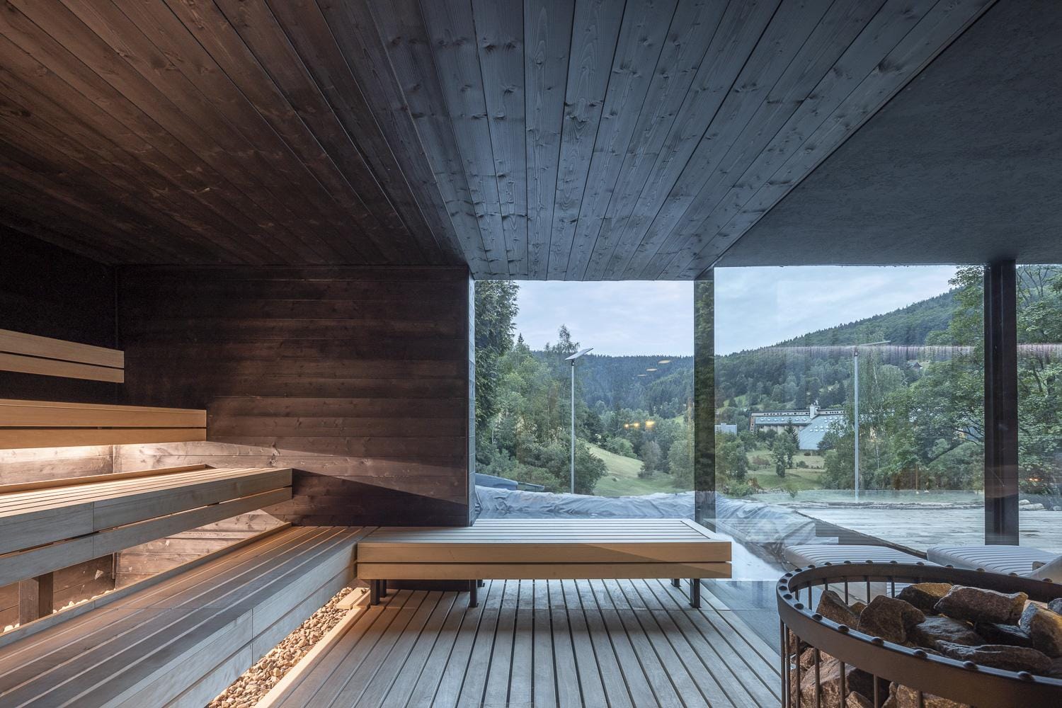 Moderne Sauna mit holzverkleideten Bänken, Panoramablick auf bewaldete Hügel.