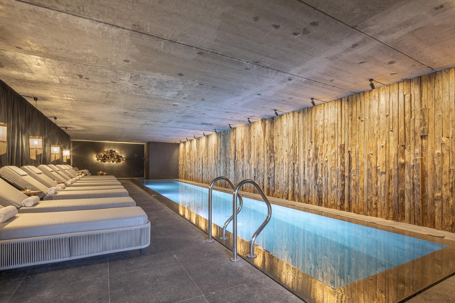 Modernes Spa mit Pool, Holzverkleidung, Liegen und gedämpfter Beleuchtung.
