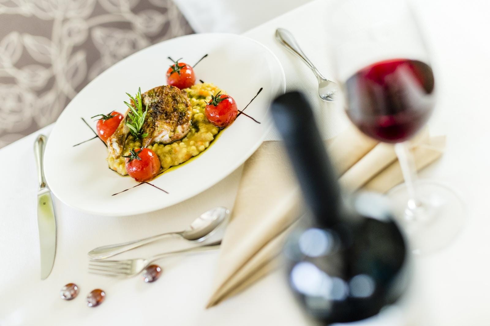 Elegant angerichtetes Gericht mit Tomaten und Fleisch, serviert mit Rotwein.