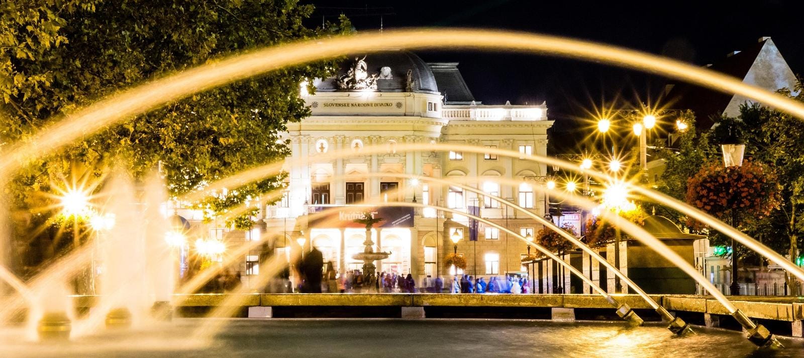 Beleuchtetes Gebäude und Brunnen in Bratislava bei Nacht, gelbe Lichter und Bögen.
