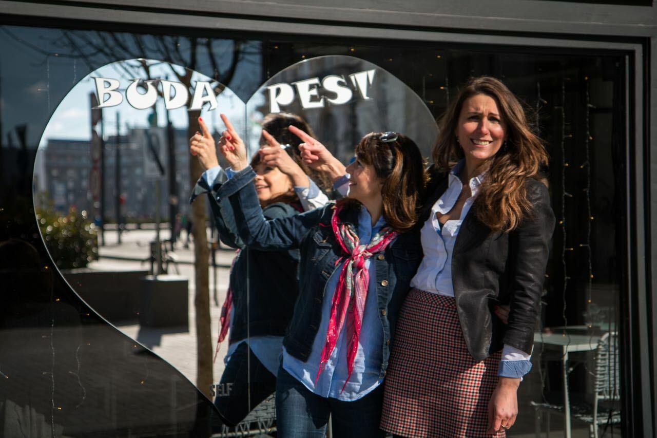 Zwei Frauen vor einem Herzspiegel mit "Budapest"-Schriftzug, fröhliche Stimmung.