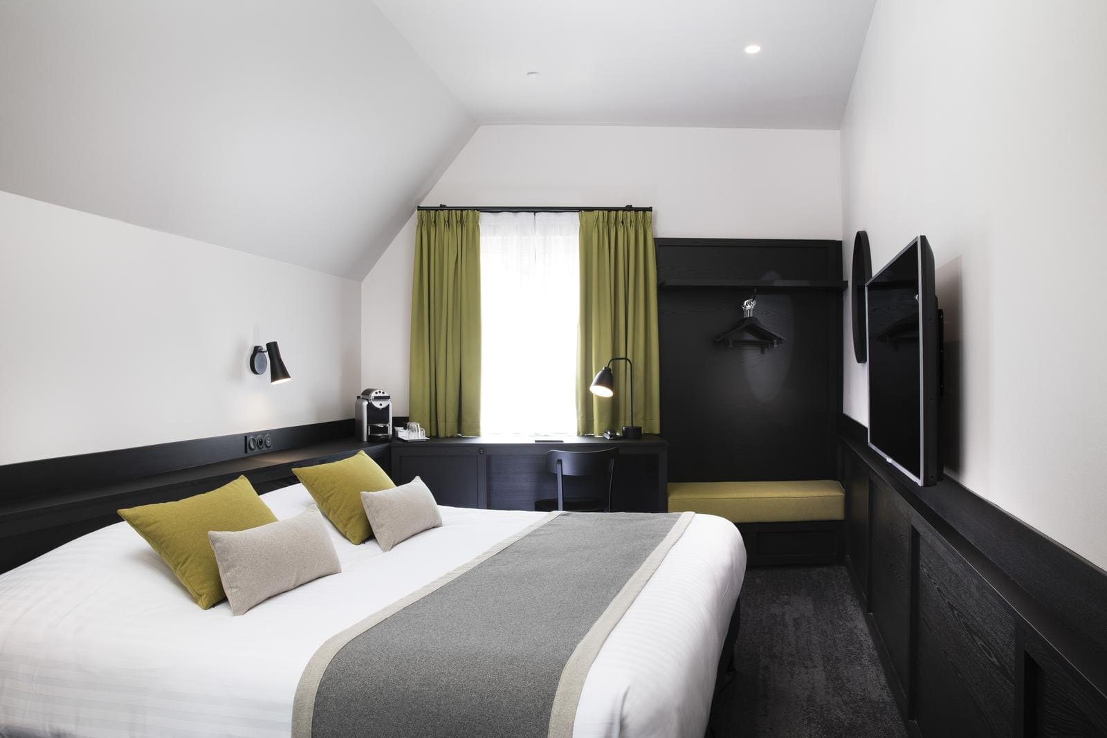 Modernes Hotelzimmer mit Doppelbett, olivgrünen Vorhängen und grauen Akzenten.