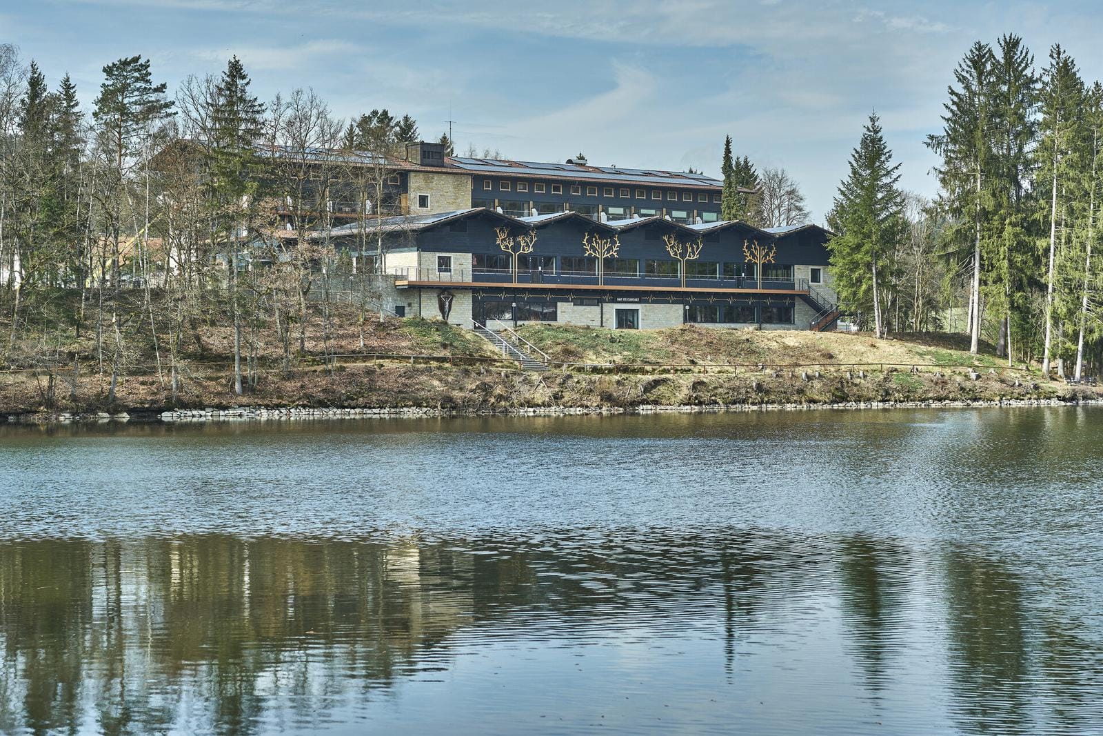 Hotel am Seeufer mit modernen Fassaden und umgeben von hohen Kiefern im ruhigen Wald.