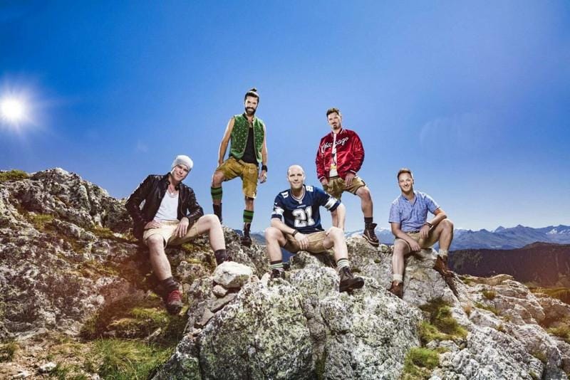 Voxxclub in bayerischer Tracht posieren auf einem sonnigen Berggipfel.