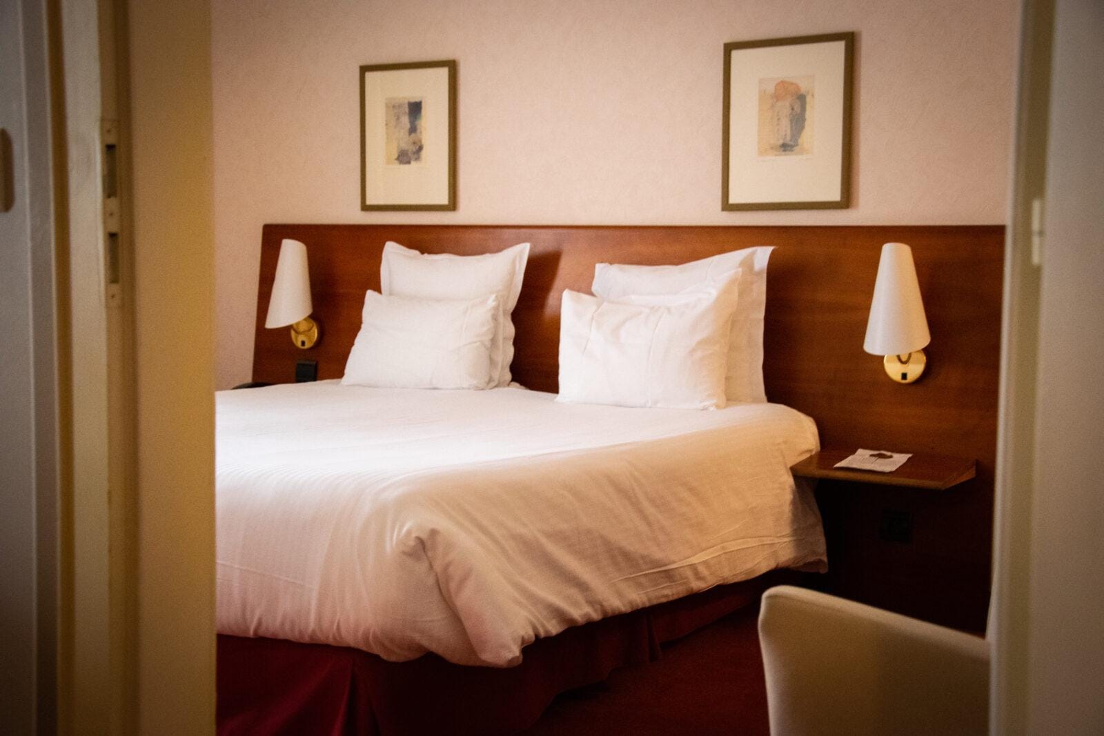 Gemütliches Hotelzimmer mit Doppelbett, Holzkopfteil, weißen Kissen und Wandbildern.