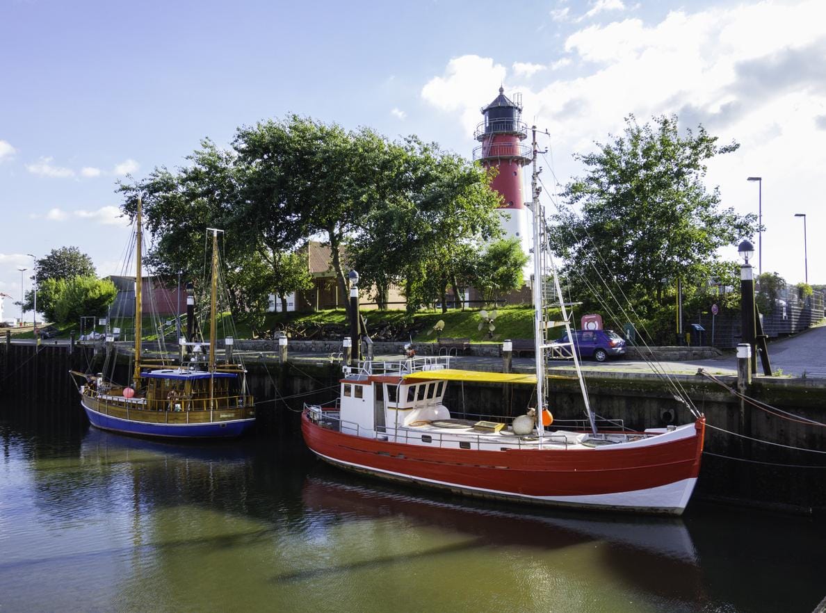 Bunte Boote im Hafen von Büsum, Deutschland, mit Leuchtturm und sonnigem Himmel im Hintergrund.