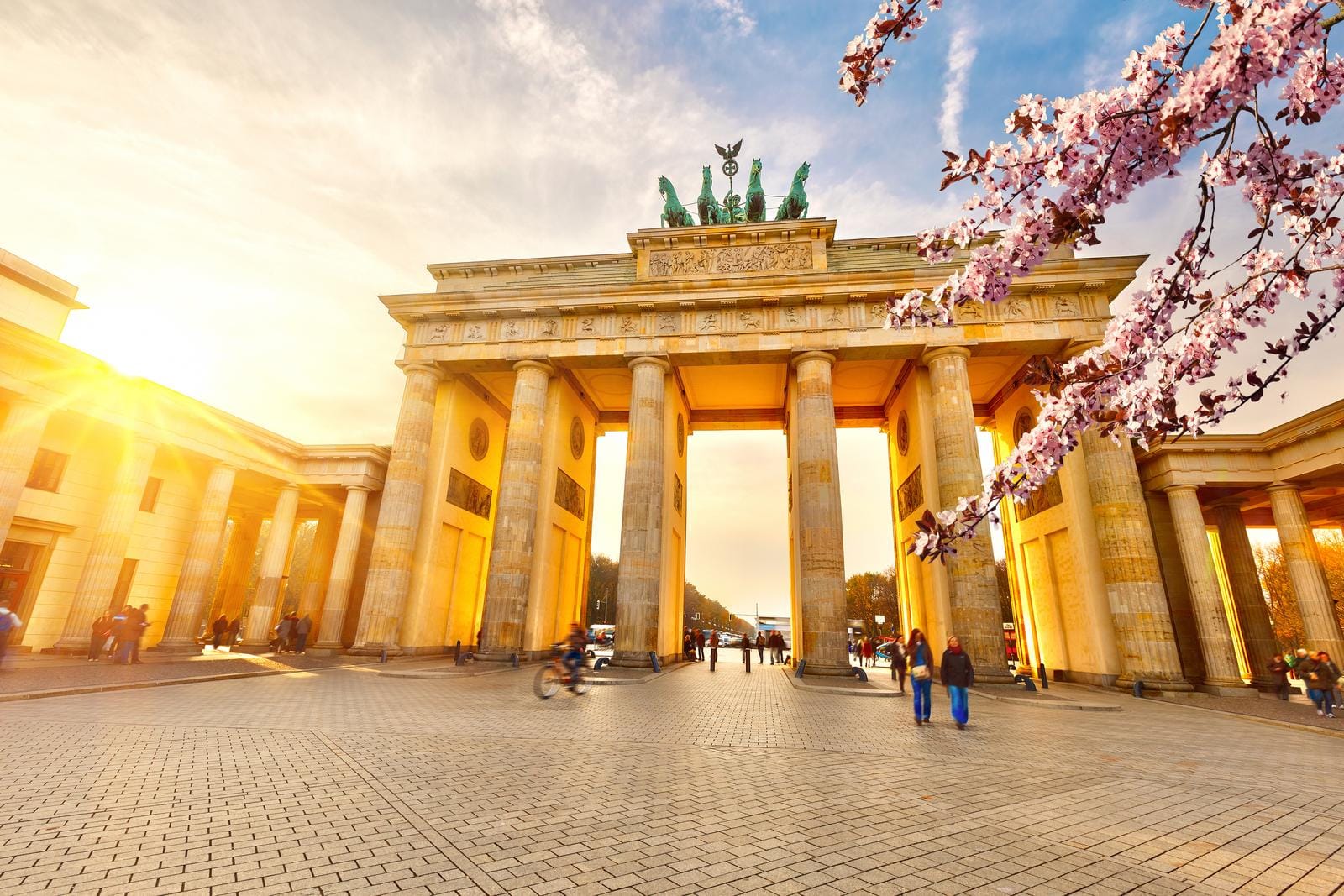 Brandenburger Tor in Berlin bei Sonnenuntergang, blühende Kirschzweige im Vordergrund.