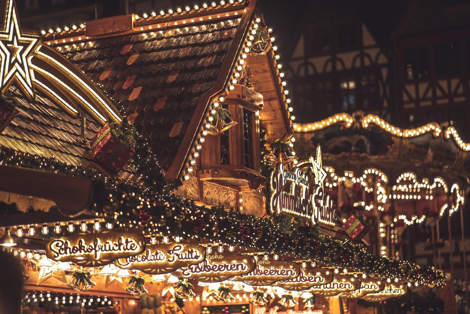 Beleuchteter Weihnachtsmarktstand mit Tannenschmuck und Schildern für Schokofrüchte.