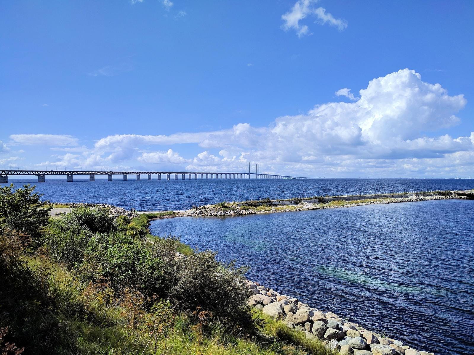Öresundbrücke über blauem Meer unter blauem Himmel mit Wolken, Küstenlandschaft im Vordergrund.